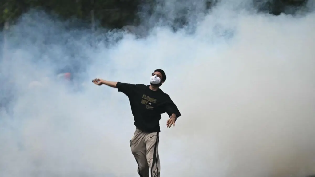 A protester throws back a tear gas canister fired by Rapid Action Force (RAF) personnel during the protest by supporters of the Cockroach Janta Party (CJP) in New Delhi on July 20, 2026.